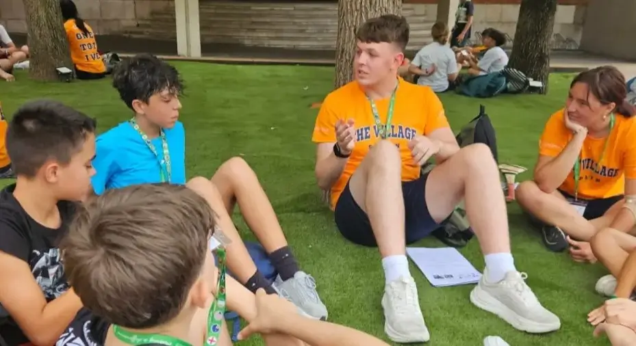 Group of teenagers chatting with an English-speaking coach at the summer camp.
