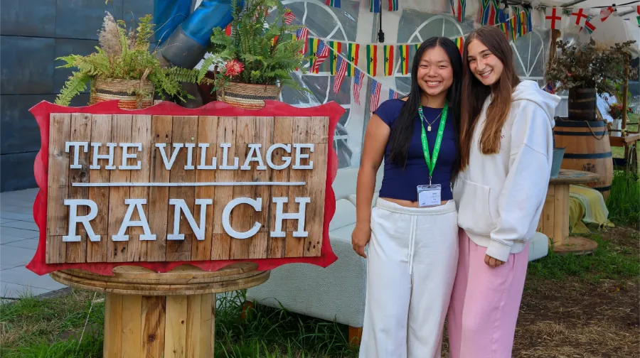 Deux filles du camp international the Village devant le panneau d'entrée de l'hôtel